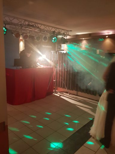 Tanzfläche mit DJ, bunten Lichtern und Rauch in einem Raum.