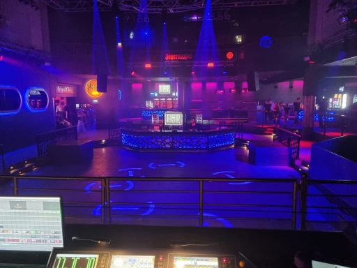 Nachtclub mit bunten Lichtern und Tanzfläche. Bühnenbereich im Hintergrund.