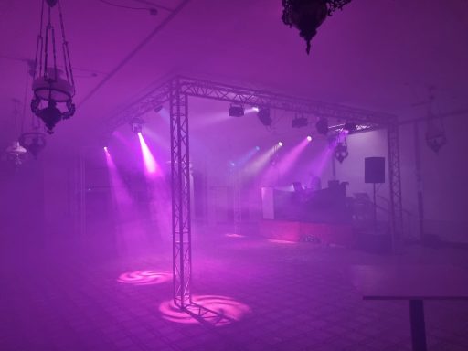 Tanzfläche mit Nebel und lila Licht, beleuchtet von Scheinwerfern in einem Veranstaltungsraum.
