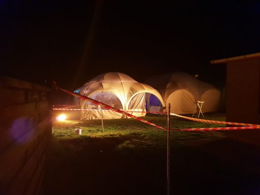 Zelte bei Nacht mit Warnbändern und orangefarbenem Licht im Hintergrund.