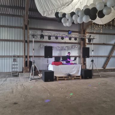 DJ-Pult mit Lautsprechern in einer Scheune, dekoriert mit Luftballons und Lichtern.
